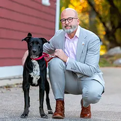 A person kneeling next to a black and white dog outside