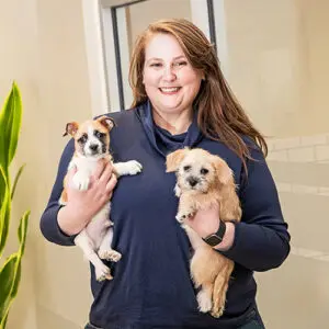 Person in a navy top holding two small puppies, one in each arm.